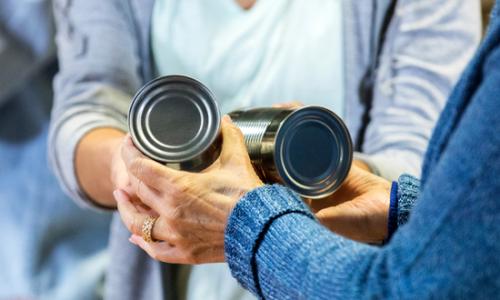 Woman passing two food tins to another person - used for the National Grid story 'Making a difference during the coronavirus outbreak'