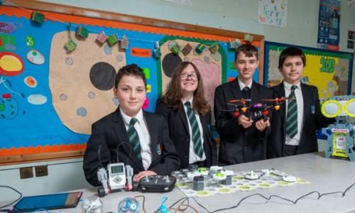 Young students wearing school uniform behind table with STEM equipment, including a drone