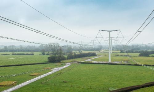 New electricity T-pylons with overhead lines across green fields
