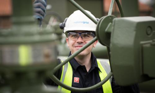 An image of a gas engineer working on-site, wearing a hard hat and a hi-vis vest