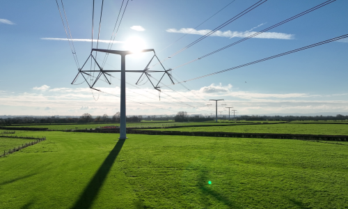 T-pylons and overhead electricity lines in the sunshine in green fields