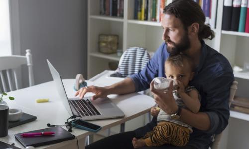 Man working on laptop holding a baby - used for the National Grid story 'Mental health comes first - especially in a crisis'