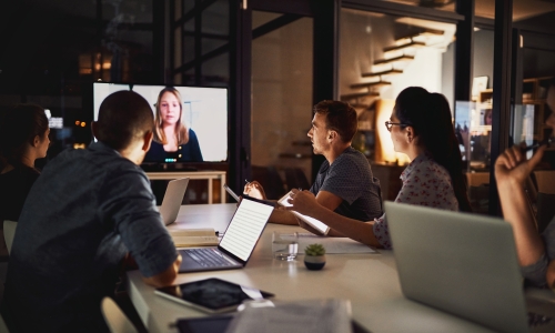 A group of individuals sitting around a table in front of a conference call screen