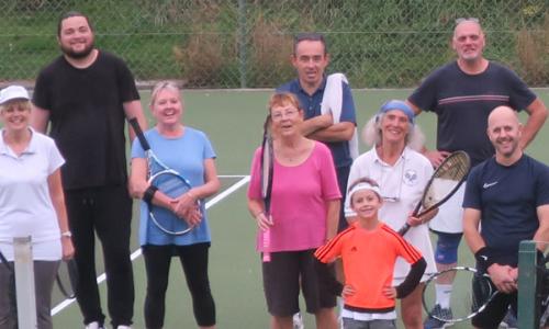 Group of people, some holding tennis rackets, on a tennis court