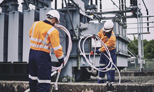 Two engineers wearing PPE coiling earth wires next to an electricity transformer