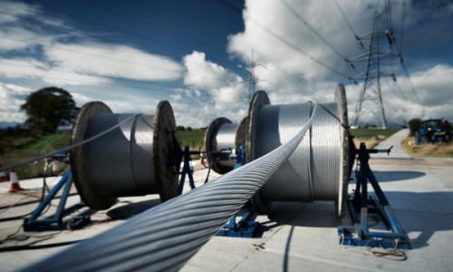 Large spools of overhead electricity lines with electricity pylon in the background