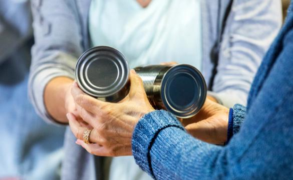 Woman passing two food tins to another person - used for the National Grid story 'Making a difference during the coronavirus outbreak'