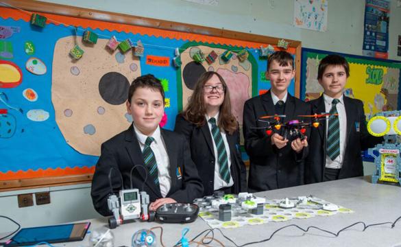 Young students wearing school uniform behind table with STEM equipment, including a drone