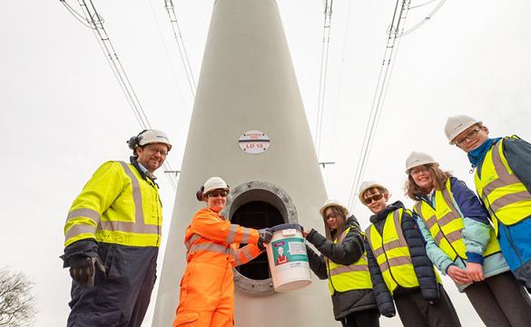 Students wearing hard hats and high-vis vests placing time capsule inside t-pylon