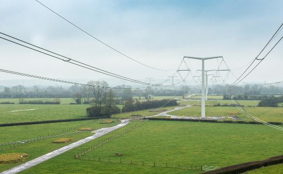 New electricity T-pylons with overhead lines across green fields