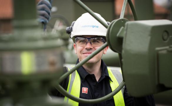 An image of a gas engineer working on-site, wearing a hard hat and a hi-vis vest