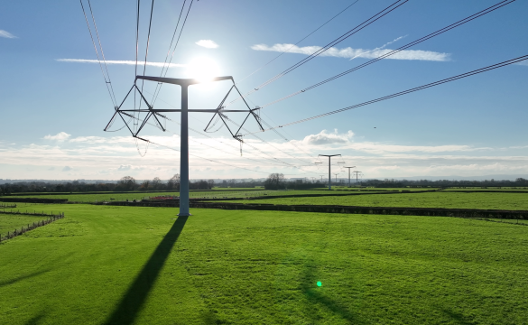 T-pylons and overhead electricity lines in the sunshine in green fields