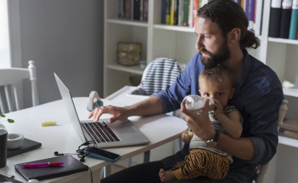 Man working on laptop holding a baby - used for the National Grid story 'Mental health comes first - especially in a crisis'