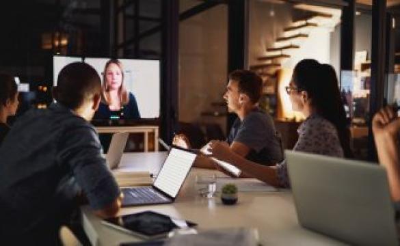 A group of individuals sitting around a table in front of a conference call screen