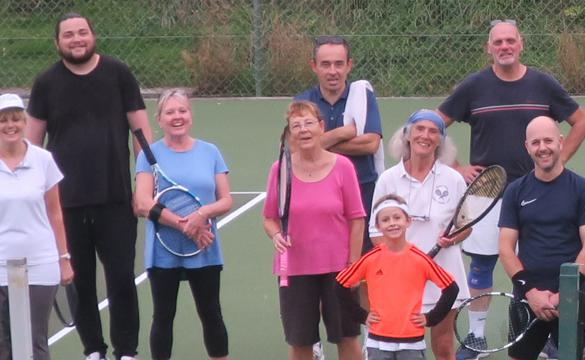 Group of people, some holding tennis rackets, on a tennis court