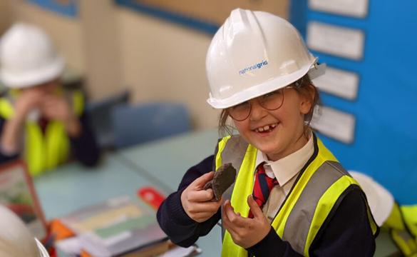 Child wearing National Grid hardhat and hi-vis vest in classroom