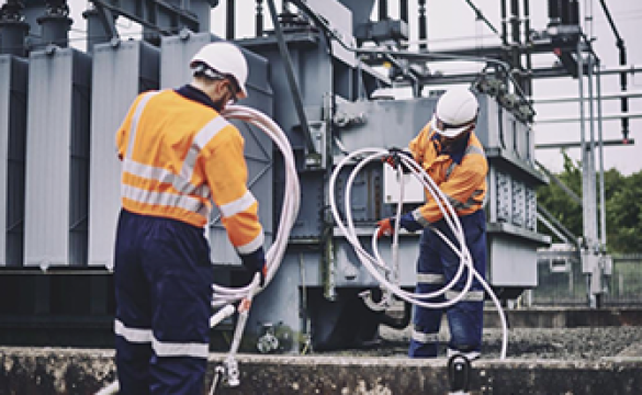 Two engineers wearing PPE coiling earth wires next to an electricity transformer