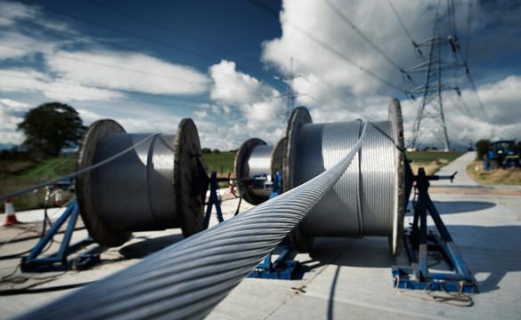 Large spools of overhead electricity lines with electricity pylon in the background
