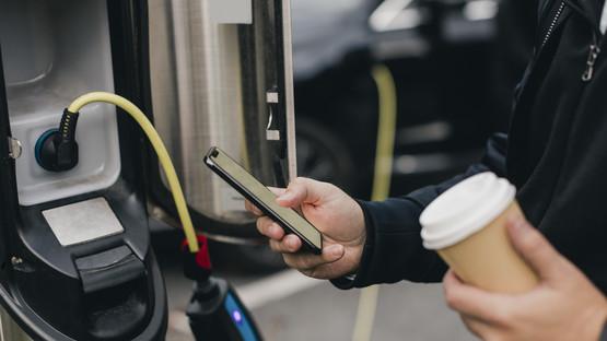 GettyImages-1252668567.jpg Person charging EV and holding coffee cup