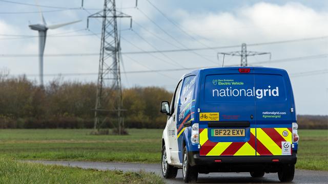 NationalGridEVVan_640x360.jpg National Grid EV van seen from behind in a field with electricity pylons and a wind turbine in the background