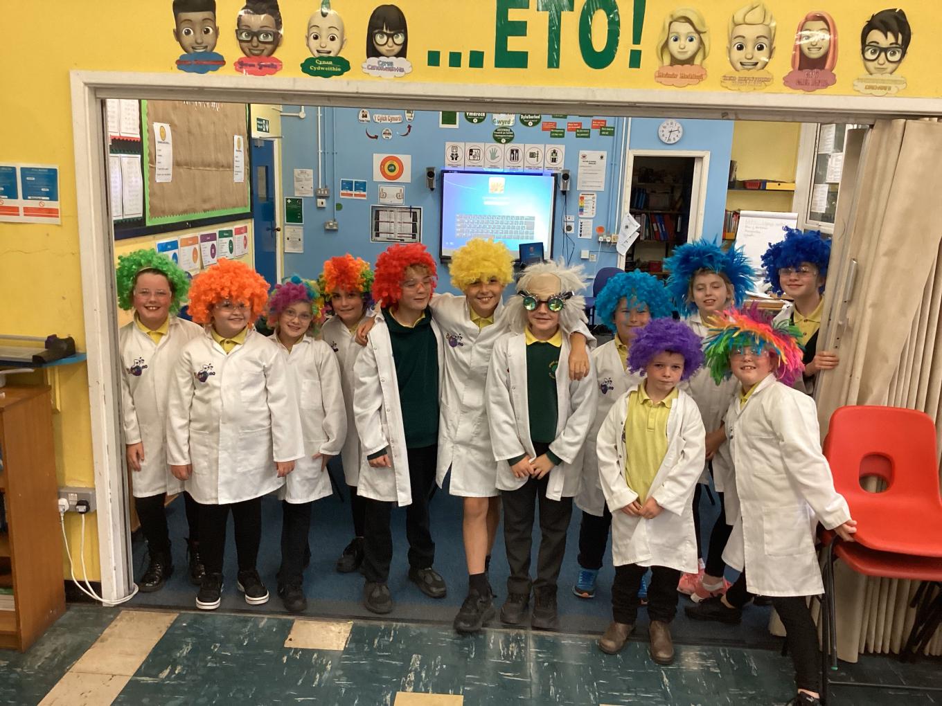 Eryri VIP schools engagement IMAGE 02 A group of children at a primary school in Wales dressed up in white lab coats and colourful wigs.